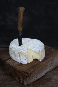 a piece of cheese on a wooden board with a knife sticking out of the top