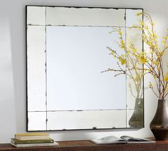 a mirror sitting on top of a wooden shelf next to a vase with yellow flowers