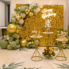 a table topped with cake and balloons next to a wall covered in gold foil decorations