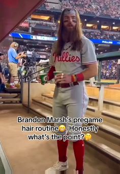 a man with long hair wearing a baseball uniform and holding a beer in his hand