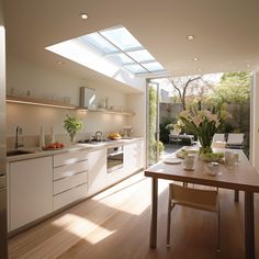 an open kitchen and dining area with white cabinets, wood flooring and skylights