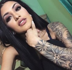 a woman with long black hair and tattoos on her arm, posing for the camera