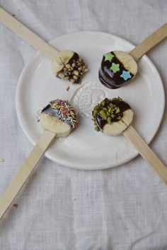 four desserts sitting on top of a white plate with wooden sticks sticking out of them