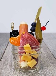 a glass bowl filled with meat, fruit and veggies on top of a wooden table