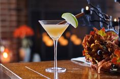 a cocktail with an apple garnish on the rim sits on a table in front of a fireplace