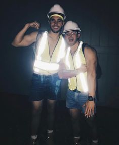 two men wearing safety vests and hard hats pose for a photo in the dark