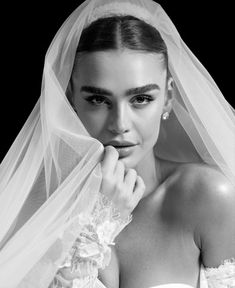 black and white photograph of a woman in wedding dress with veil over her head looking at the camera