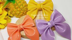 four different colored bows sitting on top of a wooden board next to flowers and pineapples