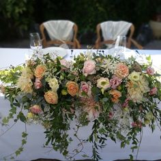 an arrangement of flowers on a table with chairs in the background