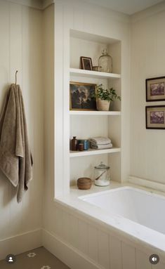 a bath tub sitting under a window next to a white shelf filled with books and pictures