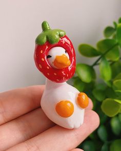 a hand holding a small toy with a strawberry on it's head and an egg in the shape of a chicken