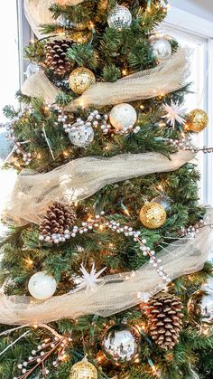 a christmas tree decorated with gold and white balls, pine cones, burlocks and ribbons