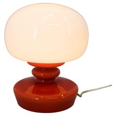 a red table lamp sitting on top of a white floor next to a light bulb