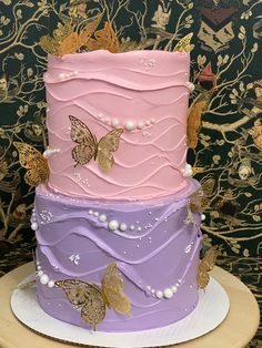 a three tiered cake decorated with butterflies and pearls is on a plate in front of a wall