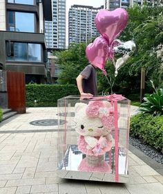 a teddy bear in a box with some balloons on the ground and a man standing next to it