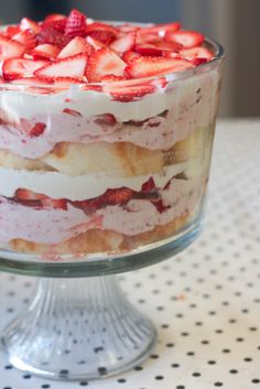 a layered cake with strawberries in it on a glass dish sitting on a polka dot tablecloth