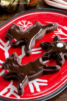 three chocolate reindeer cookies on a red plate with white snowflakes and candy canes