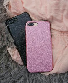 two iphone cases sitting on top of a fur covered bed next to each other, one black and the other pink