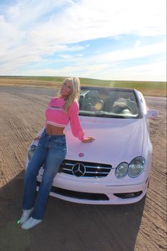 a woman leaning on the hood of a white car with her arms out in front