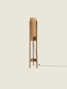 a wooden floor lamp with a beige shade on it's side and a cord attached to the base