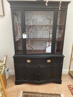 a black china cabinet sitting on top of a tiled floor