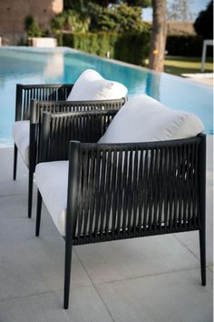 two black chairs sitting next to a pool with white pillows on it's back