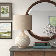 a white vase sitting on top of a wooden dresser next to a mirror and lamp