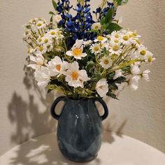 a blue vase filled with lots of white and yellow flowers on top of a table