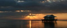 the sun is setting over an ocean with a house on stilts in the water