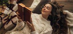 a woman is laying on the floor reading a book next to presents and a christmas tree