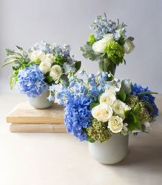 three vases filled with blue and white flowers on top of a wooden table next to a book