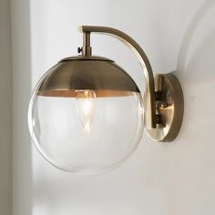 a wall light with a clear glass ball hanging from it's arm and an antique brass finish