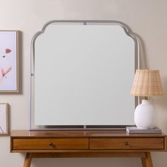 a mirror sitting on top of a wooden table next to a lamp and pictures hanging on the wall