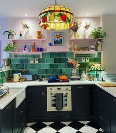 a kitchen with black cabinets and green tile backsplash, white countertops and an oven in the center