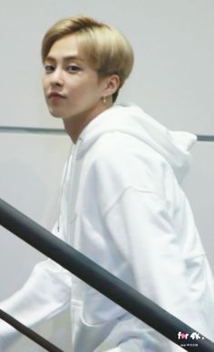 a young man with blonde hair wearing a white hoodie and black pants, walking up some stairs