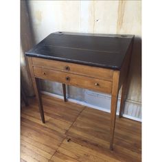 an old wooden desk sitting on top of a hard wood floor next to a wall