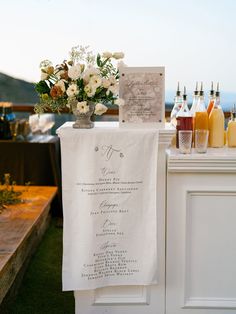 a table set up with drinks and menus for an outdoor wedding reception on the grass