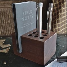 a pen holder with two pens and a notebook in it on top of a table