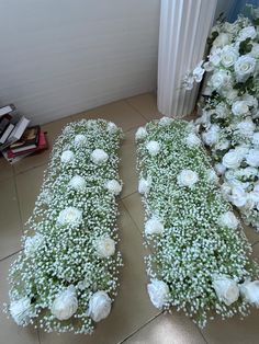 two rows of white flowers on the ground next to a radiator and books