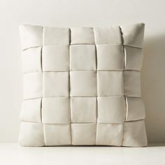 a white pillow made out of square pieces of leather, on a table in front of a wall