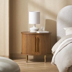 a nightstand with a lamp on top of it next to a bed in a room