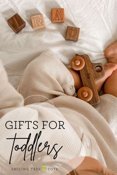 a baby laying on top of a bed next to wooden blocks with words that read gifts for toddlers