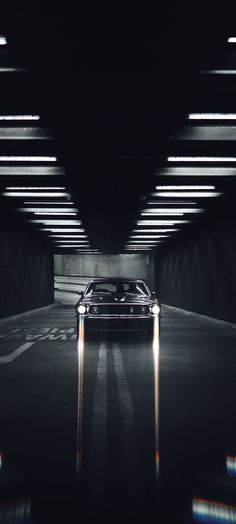 a car driving through a dark tunnel with lights on the floor and in front of it