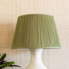 a white table lamp with a green shade on it next to a potted plant