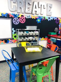 there is a black table with colorful chairs around it and a chalkboard on the wall