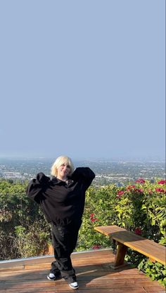 a woman standing on top of a wooden deck next to a bench with her arms behind her head