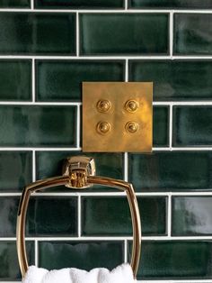 a gold towel holder with three brass knobs on the side of a green tiled wall