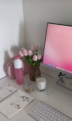 a desktop computer sitting on top of a desk next to a vase with flowers in it