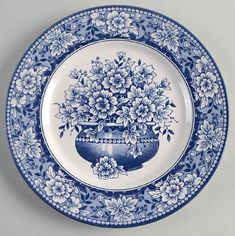 a blue and white plate with flowers in a vase on the bottom, sitting on a table