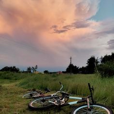 two bikes are sitting in the grass under a pink sky with clouds above them and one is upside down